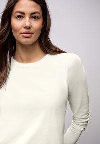 Lichtcrème lange mouw top met een ronde halslijn en licht geplooide schoudernaden. Glad, zacht materiaal met een ontspannen pasvorm.