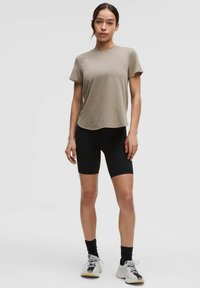 Beige short-sleeve t-shirt paired with black bike shorts. Model wearing white and black sneakers. Smooth fabric with a relaxed fit.