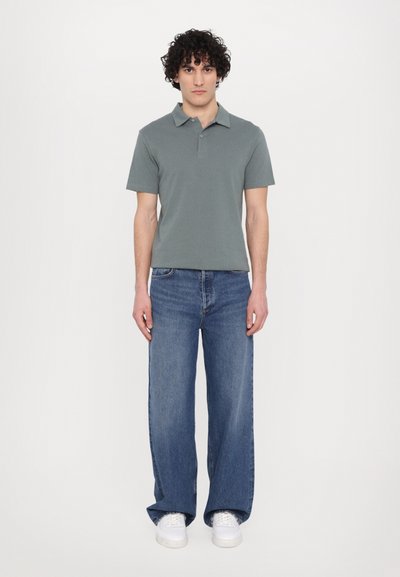 Green short-sleeve polo shirt with a classic collar, paired with wide-leg blue denim jeans and white sneakers. Simple design, casual fit.