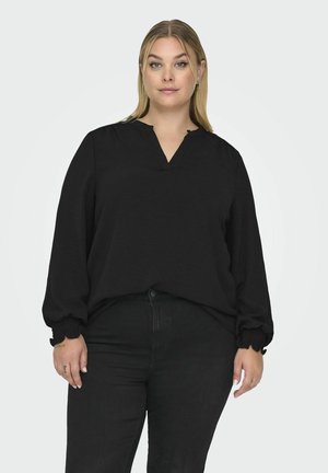 Sort langærmet bluse med V-udskæring, gummistropper og løs pasform, lavet af blødt materiale. Sat sammen med sorte jeans.