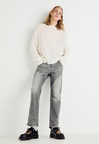 Oversized, ribbet, kremfarget genser kombinert med rette, falmede grå jeans og svarte snøresko med et mønsterdetalj på tungen.