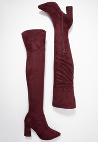 Botas altas color burdeos de ante, con punta afilada, tacón ancho y cremallera lateral para facilitar su uso.