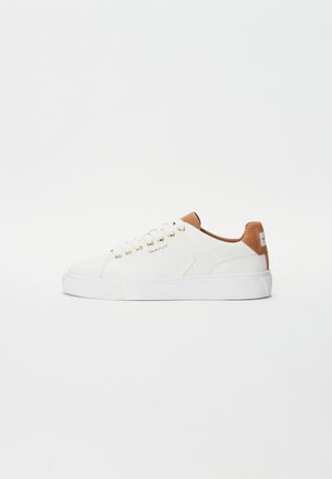 Hvite skinnsko med en beige lærdetalj på hælen, gulløyler og en tykk hvit gummisåle. Enkelt, minimalistisk design.