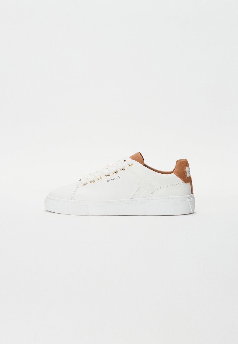 White leather sneakers with a tan leather accent on the heel, gold eyelets, and a thick white rubber sole. Simple, minimalist design.