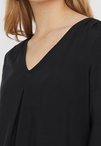 Schwarze Bluse mit V-Ausschnitt, aus weichem Stoff, mit Faltenstruktur an der Vorderseite und kurzen Ärmeln, die eine lässige Silhouette schaffen.