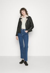 Casaco de couro preto com gola de pelagem, blusa de tom claro, jeans azuis de cintura alta e tamancos pretos com tachas prateadas.