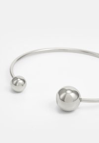 Pulsera de pulsera de metal plateado que presenta dos extremos esféricos. Textura suave con un diseño minimalista y un grosor uniforme.