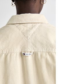 Beige kordflöjlskjorta med krage och vertikal ribbad textur. Har en liten "TOMMY JEANS"-etikett på baksidan.