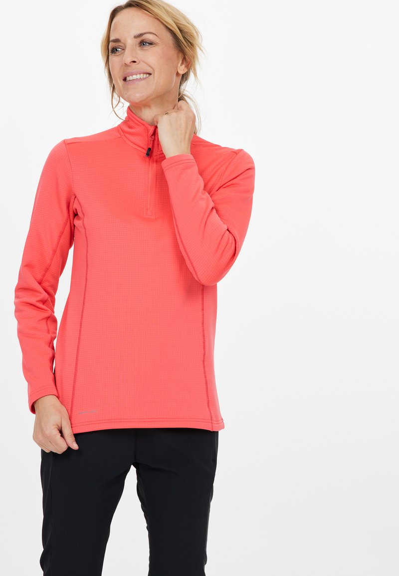 Roter Langarmpullover mit halb-gezipptem Kragen, strukturiertem Stoff und kontrastierenden Nähten, kombiniert mit schwarzen Hosen.