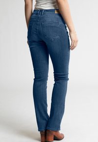 Lieknos mėlynos džinsinės kelnės su vidutinio aukščio juosmeniu, turinčios galinius kišenes ir lygų paviršių. Avimos rudos su kniedėmis botais.