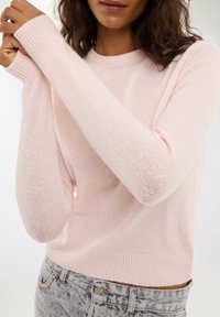 Maglione lavorato a maglia rosa chiaro con polsini e orlo a costine. Il tessuto presenta una texture leggera e morbida, con un semplice scollo rotondo.