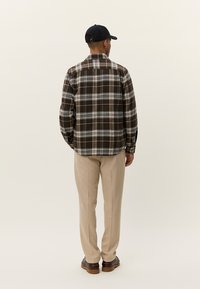 Braun-weiße karierte Button-Up-Hemd mit langen Ärmeln, kombiniert mit beigen Hosen. Der Stoff wirkt strukturiert und hat eine lockere Passform.