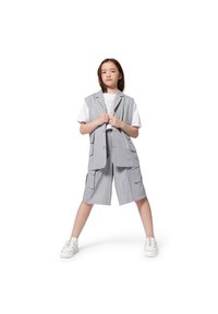 Grijze linnen gilet met korte cargoshorts en een wit graphic t-shirt. Witte sneakers. Rechte houding met de handen die het gilet vasthouden.