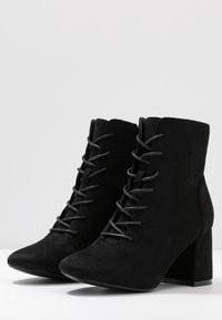 Stivaletti neri in suede fino alla caviglia con tacco a blocco, lacci frontali, texture liscia e punta affusolata. Design semplice, senza marchi o motivi visibili.