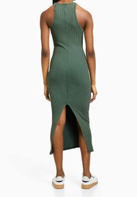 Vestito midi verde a coste con spacco alto sul retro, caratterizzato da un design aderente e scollo tondo. Abbinato a sneakers bianche.