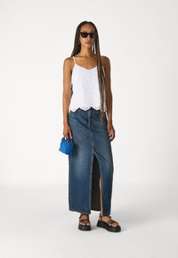 White eyelet cropped top with scalloped hem, paired with a blue denim maxi skirt featuring a front slit. Adds a blue mini bag and black sandals.