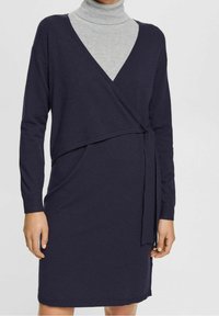 Marinblå omslagsklänning med långa ärmar, tillverkad av mjukt trikåtyg, med en knytning i midjan och en kontrasterande grå polokrage under.