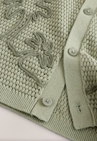 Light green knitted cardigan featuring a textured pattern, embroidered detail, and large buttons. Includes ribbed accents at the edges.