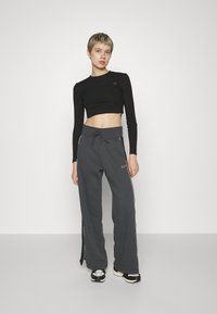 Black cropped long-sleeve shirt paired with dark gray wide-leg sweatpants featuring white side stripes and a drawstring waist.