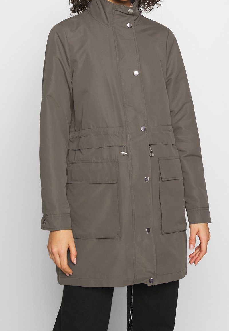 Grå knälång jacka i syntetmaterial med hög krage, tryckknappar och två framfickor. Har justerbar dragsko i midjan.