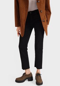 Blazer in suede marrone sopra una maglia bianca, abbinato a jeans neri cropped e scarpe marroni con lacci e suola nera spessa.
