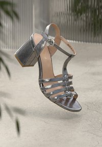 Metallic silberne Sandale mit Absatz, offenem Zehenbereich, verstellbarem Knöchelriemen, horizontalem Riemendesign und klobigem Absatz. Glatte, glänzende Oberfläche.