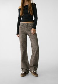 Černý top s odhalenými rameny a dlouhými rukávy, doplněný hnědými kalhotami s leopardím potiskem a širokými nohavicemi. Tenisky se vyznačují kontrastními tkaničkami a texturovaným povrchem.