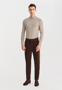 Beżowy dopasowany golf i ciemnobrązowe sztruksowe spodnie z wysokim stanem i bocznymi kieszeniami, w połączeniu z brązowymi eleganckimi butami.