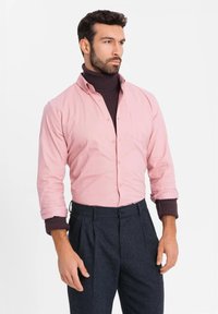 Lichtroze overhemd met lange mouwen, gecombineerd met een donkere coltrui. Donkergrijze geplooide broek. Focus op klassieke snit en texturen.