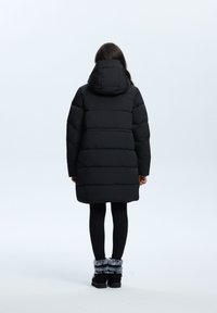 Zwarte gewatteerde jas met een capuchon, met een doorgestikt ontwerp en een lengte tot halverwege de dijen. Draag het over zwarte leggings en enkellaarsjes met fuuraccenten.