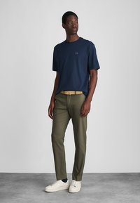 Tricou din bumbac navy, croială relaxată. Pantaloni verzi măslinii, cu picior drept. Curea bej, adidași albi. Design minimalist, fără modele vizibile.