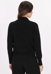 Cardigan negru din tricot, cu tiv și manșete cu dungi, având un guler înalt și o textură moale, prezentat din spate.