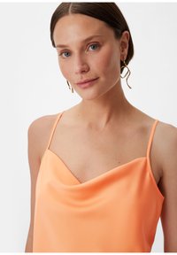 Brzoskwiniowa satynowa koszulka na ramiączkach z dekoltem w kształcie łódki, o gładkiej fakturze i luźnym kroju.