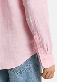 Lichtroze linnen shirt met lange mouwen, getopt met knopen, en een gebogen rand, gecombineerd met lichtblauwe denim jeans.