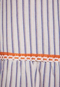 Tessuto a righe con linee verticali blu e arancioni su uno sfondo beige, accentuato da un dettaglio all'uncinetto arancione e bianco all'orlo.