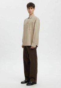 Beige, stripet langermet skjorte med knapper og brystlomme, kombinert med løse brune bukser og svarte sko. Minimalistisk design med myk tekstur.