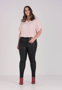 Light pink V-neck top, loose fit; black shiny leather-like skinny pants; red ankle boots. Smooth texture and casual design.