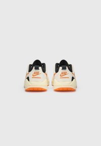 Bijele i crne atletske tenisice s narančastim detaljima, s teksturiranom gornjom površinom, obloženim potplatom i Nike logom na peti.