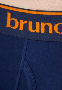 Granatowe bokserki z pomarańczowym logo "bruno" na elastycznym pasku. Materiał wydaje się gładki, z prążkowaną fakturą i płaskimi szwami.