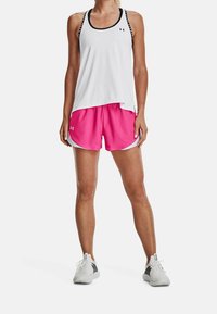 Vit träningslinne med svarta detaljer, kombinerat med rosa shorts med vita kanter. Modellen har på sig grå sneakers som visar en bekväm passform.