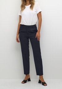 Navy skräddarsydda byxor med smal passform, med sidofickor, platt front och en slät textur, kombinerade med en vit t-shirt och svarta mules.