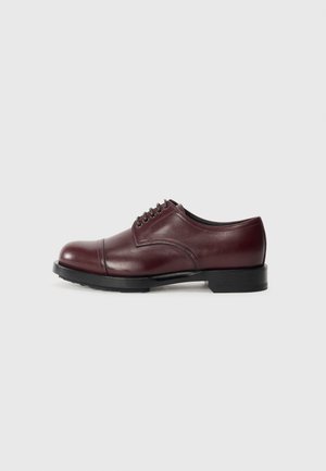 Sapato de pelica burgundy com bico arredondado e design de bico de metal. Sola preta com salto baixo e cinco ilhós paralelos para os atacadores.