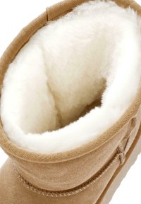 Botte d'hiver en suède camel avec une doublure en molleton blanc pelucheux visible à l'intérieur de la tige.