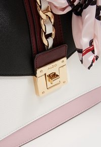 Czarnobiała torebka z fakturą z bordowym akcentem, złotym okuciem oraz wzorzystym różowym szalikiem jedwabnym jako ozdobą. Posiada zapięcie na kwadratową blokadę.