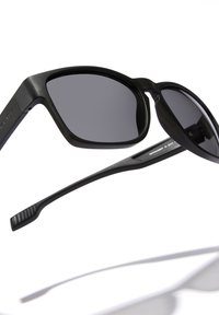 Must ikk sunglasses tumedate läätsedega, ristkülikukujuline raam, sile tekstuur ja kerge disain. Omab tekstuuriga temppe, et tagada kinnitamine.