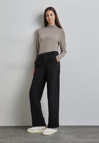 Beige Strickkragenpullover kombiniert mit schwarzen, maßgeschneiderten Hosen. Die Hose zeichnet sich durch ein elegantes Design mit einer vorderen Knopfleiste und Taschen aus.