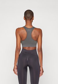 Soutien-gorge de sport gris avec un design dos nageur, fabriqué à partir d'un matériau extensible. Associé à un legging noir taille haute avec un logo sur la ceinture.