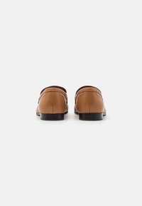 Mocassins en cuir marron avec une finition lisse, un dos arrondi et un design minimaliste. Dotés d'un petit talon noir pour la stabilité.