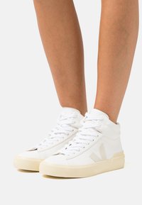 White high-top sneakers made of leather, featuring a textured finish, round toe, flat lace-up design, and a cream rubber sole.