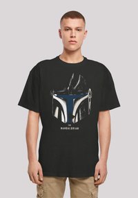 Svart t-skjorte med grafikk av et hjelm, med blå og hvite detaljer og teksten "THE MANDALORIAN" under.